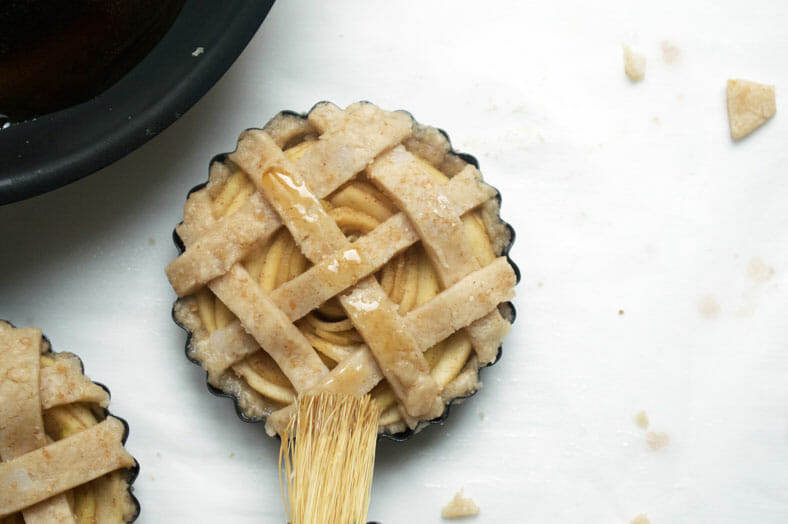 brushing the lattice top of vegan apple pie with the extracted juices from sliced apples