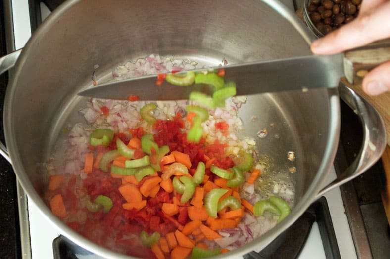 To make Moro de Guandules, a traditional Dominican Pigeon Peas Rice dish, you'll start by heating up some oil to deep pan and then adding garlic, onion, red pepper, carrots and celery