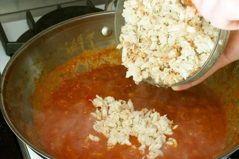 Adding crab meat into the stew of tomato, chili, garlic and shallots for Singapore's chili crab dish