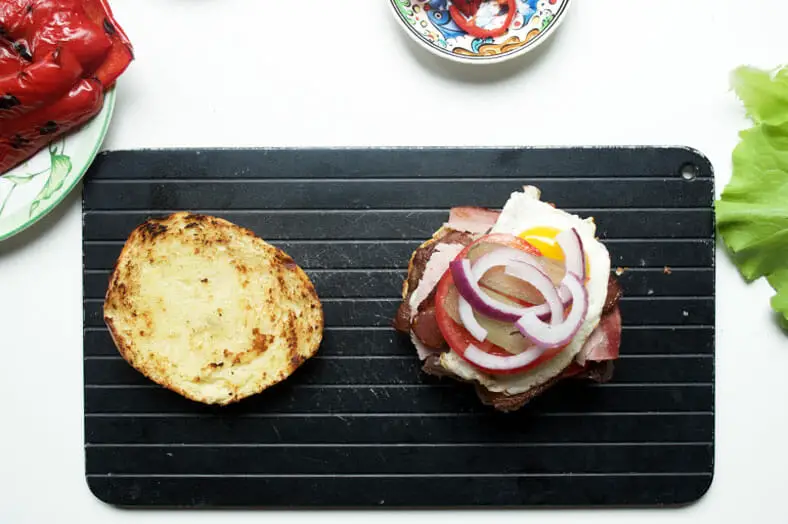 Once you have prepared and grilled the meats and other ingredients need to build the Uruguayan Chivito sandwich, start with the bun as the base and build up. Here we started with skirt steak on the bottom, then cheese, roasted red pepper, ham, bacon, fried egg, tomato, pickles and red onions
