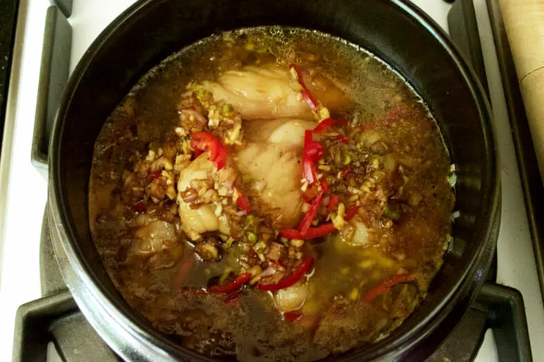 To finish making Ca Kho To, a Vietnamese caramelized fish stew, on top of the layers of shallots and garlic, white fish, marinade and coconut water, you will add some fresh chilis, ground black pepper and your caramel sauce, and then let everything sit and simmer over medium-low heat for 15 minutes